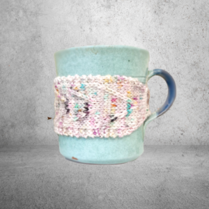 A teal mug is wrapped with a pink speckled hand-dyed merino mug cozy