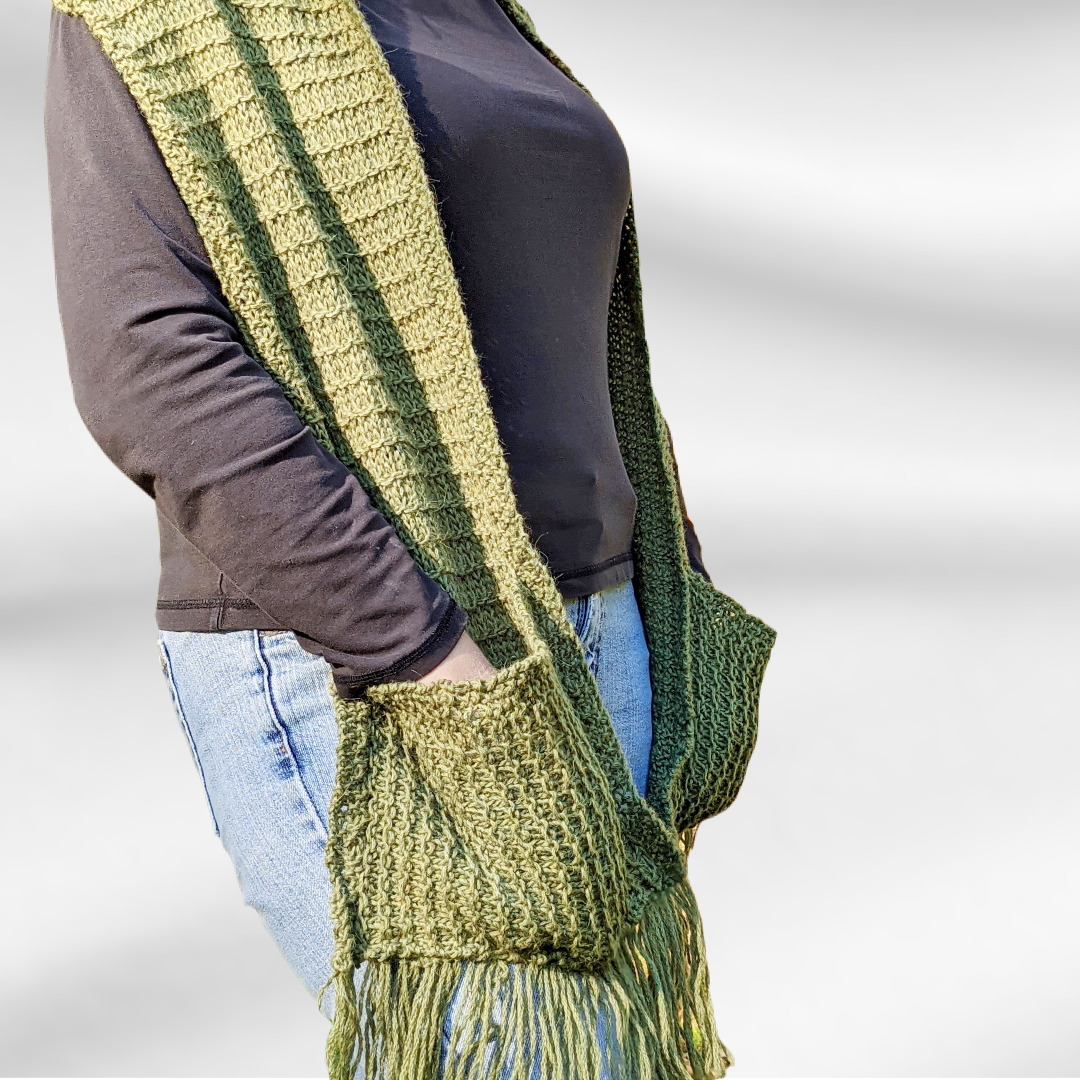A woman is shown wearing a mossy green oversized scarf with pockets and fringe on both ends