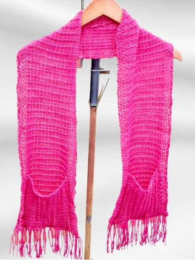 A hand dyed merino fuchsia scarf hangs draped around a hanger. The scarf has oversized pockets and fringe on each end