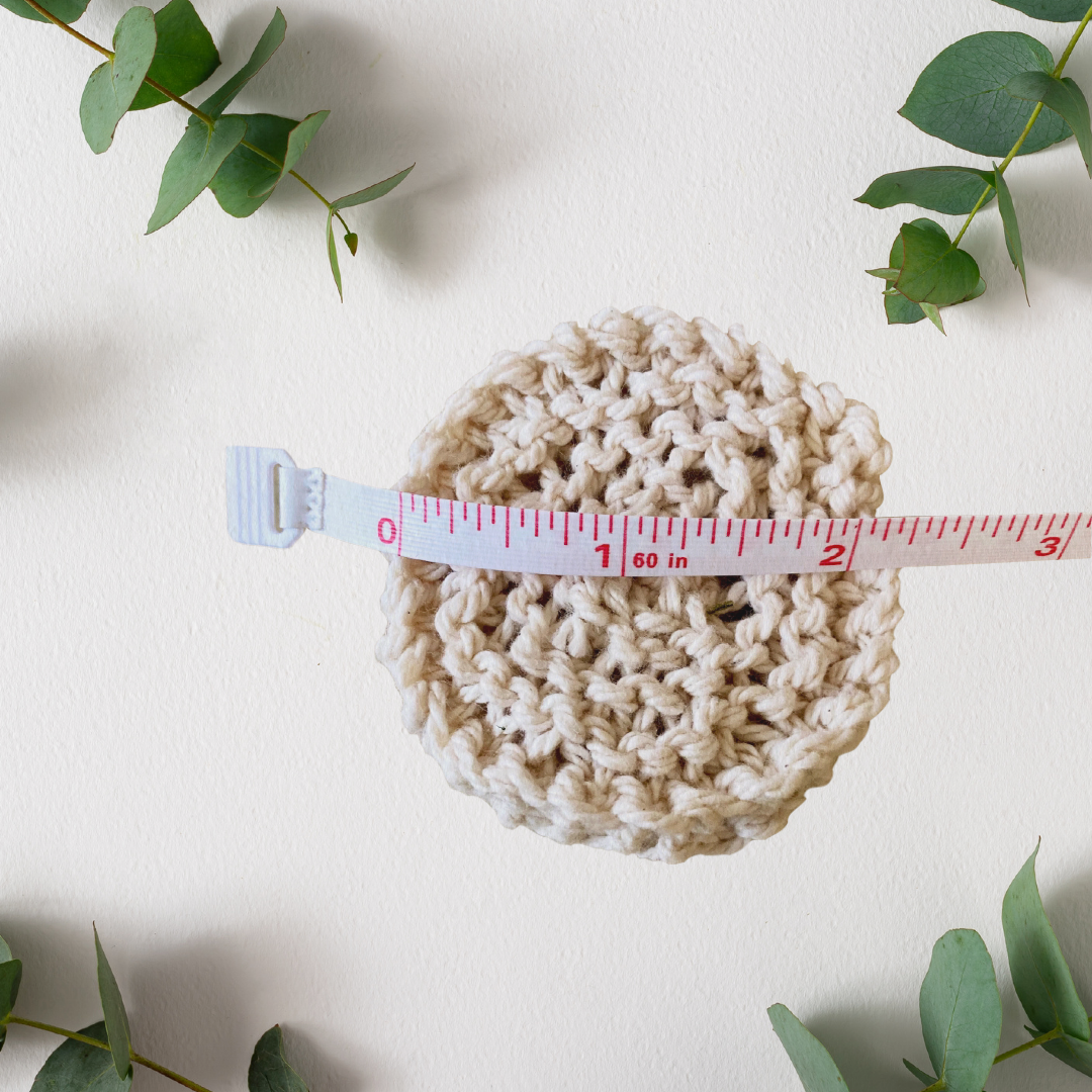 A Virginia-grown cotton reusable facial round is shown with a measuring tape showing they are approximately 2.25 inches across. A sprig of eucalyptus is in each of the four corners