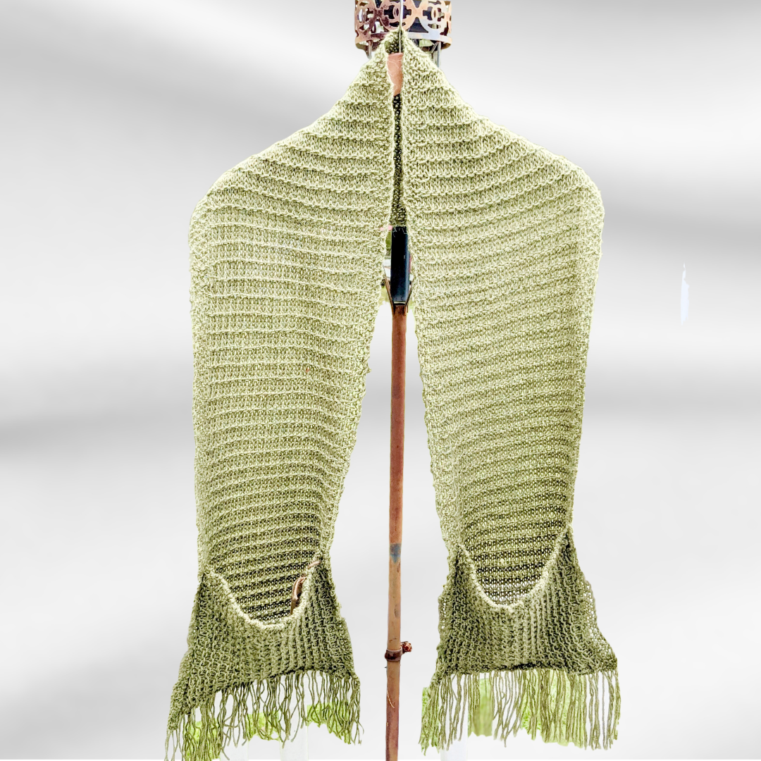 A mossy green scarf hangs from a hanger on a stand. It is an oversized scarf with pockets and fringe on each end