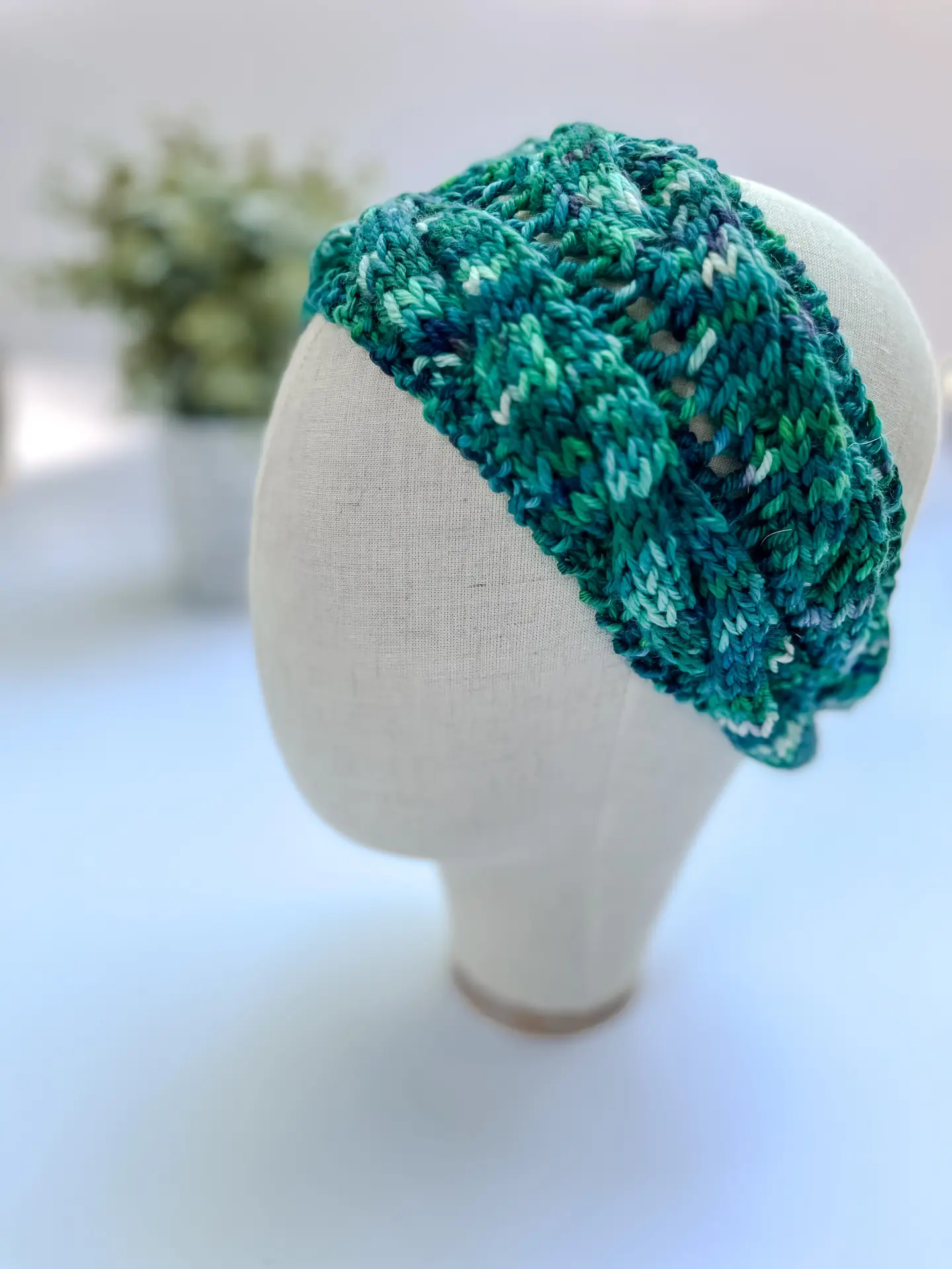 A teal, hand-dyed merino ear warmer headband is displayed on a cloth mannequin head.