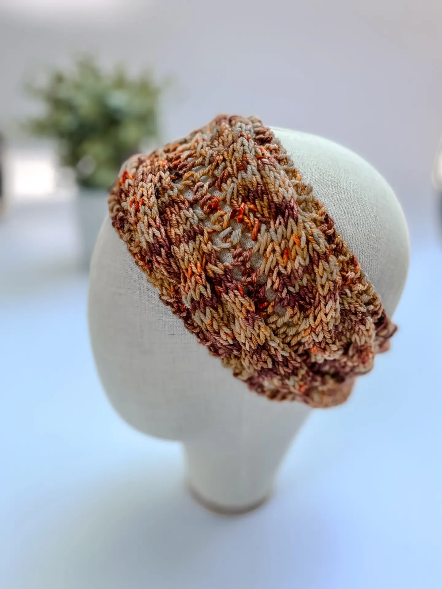 A hand-dyed merino ear warmer headband in a variety of fall colors, is displayed on a cloth mannequin head.