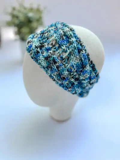 A blue, white and gray, hand-dyed merino ear warmer headband is displayed on a cloth mannequin head.