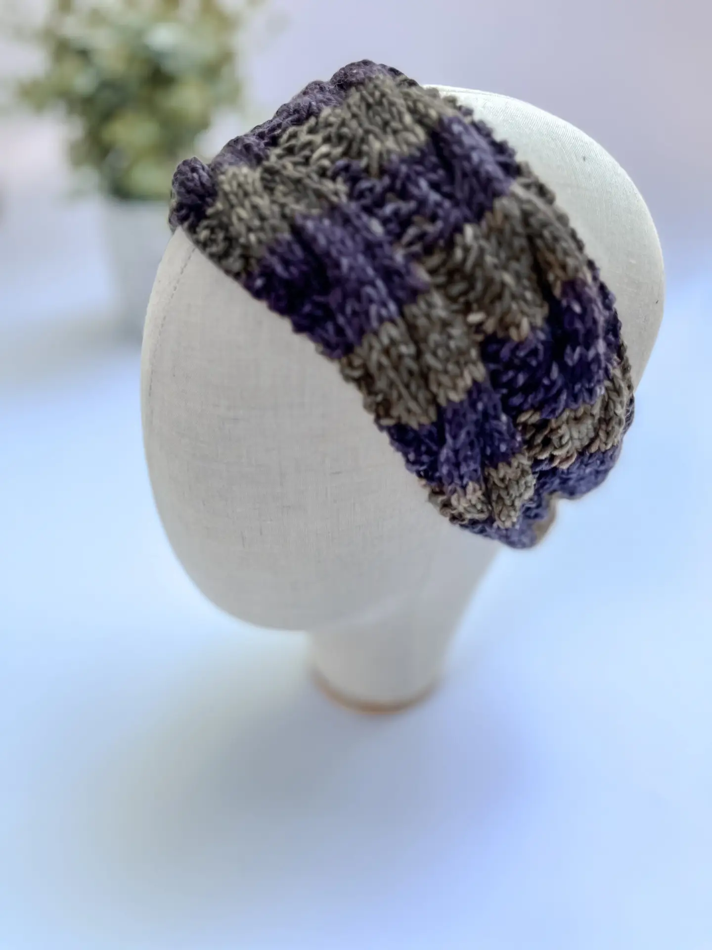 A green, brown, charcoal and gray striped, hand-dyed merino ear warmer headband is displayed on a cloth mannequin head.