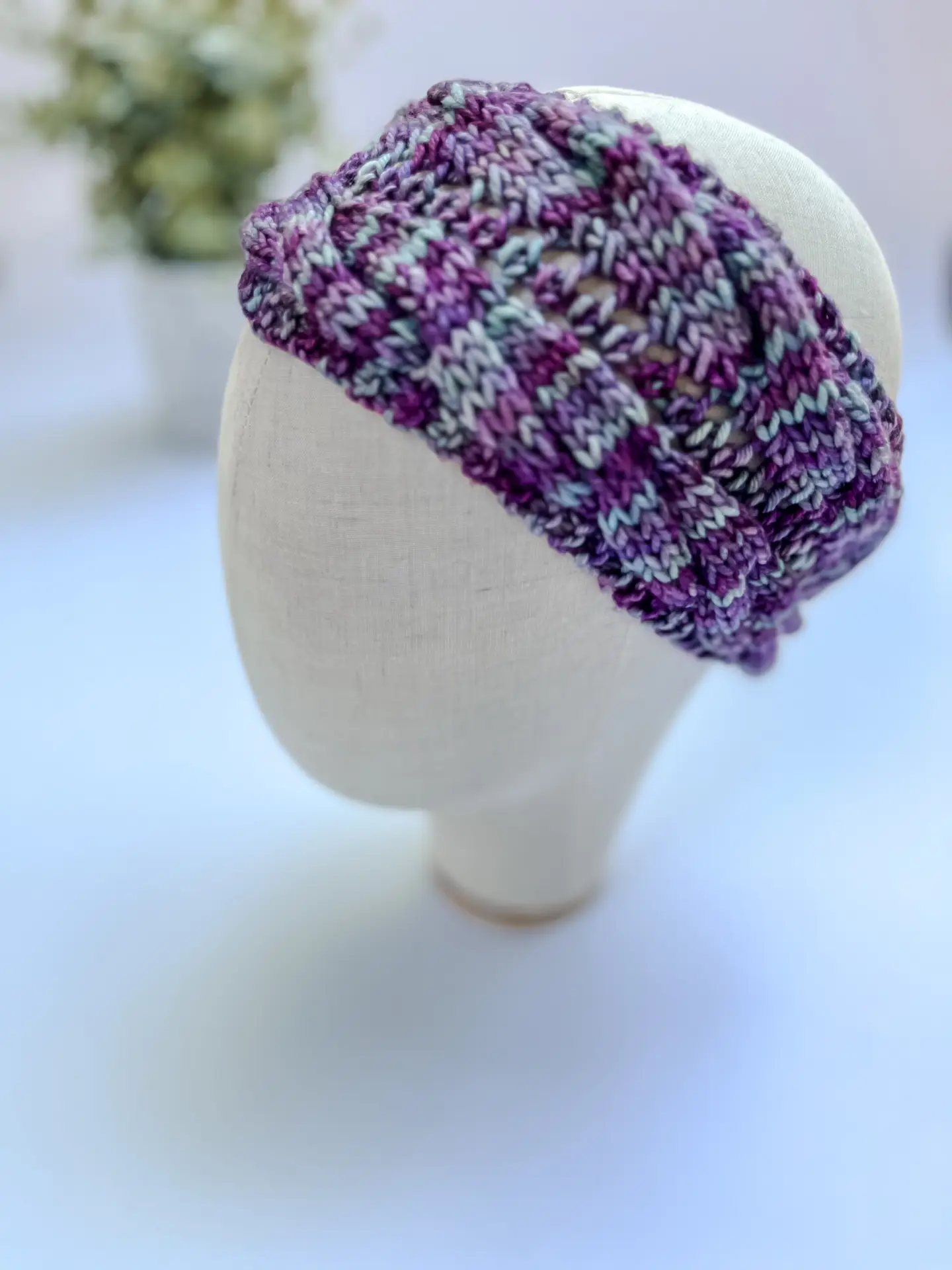 A teal, purple, blue, and gray hand-dyed merino ear warmer headband is displayed on a cloth mannequin head.