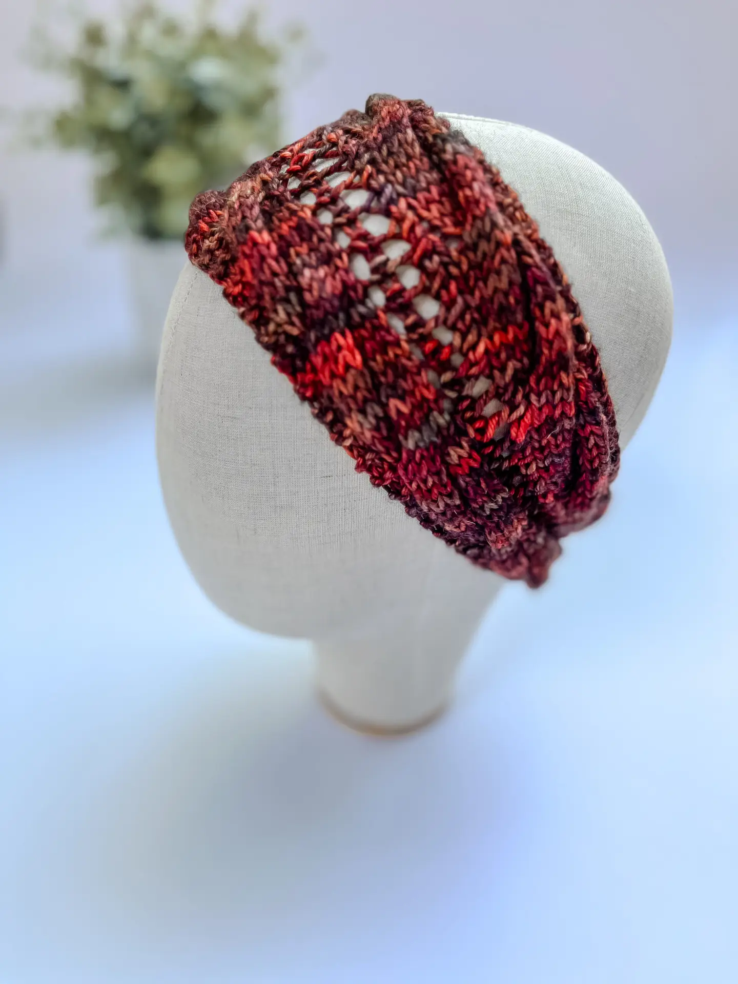 A hand-dyed merino ear warmer headband in a variety of rich fall colors including oranges, reds, and browns, is displayed on a cloth mannequin head.