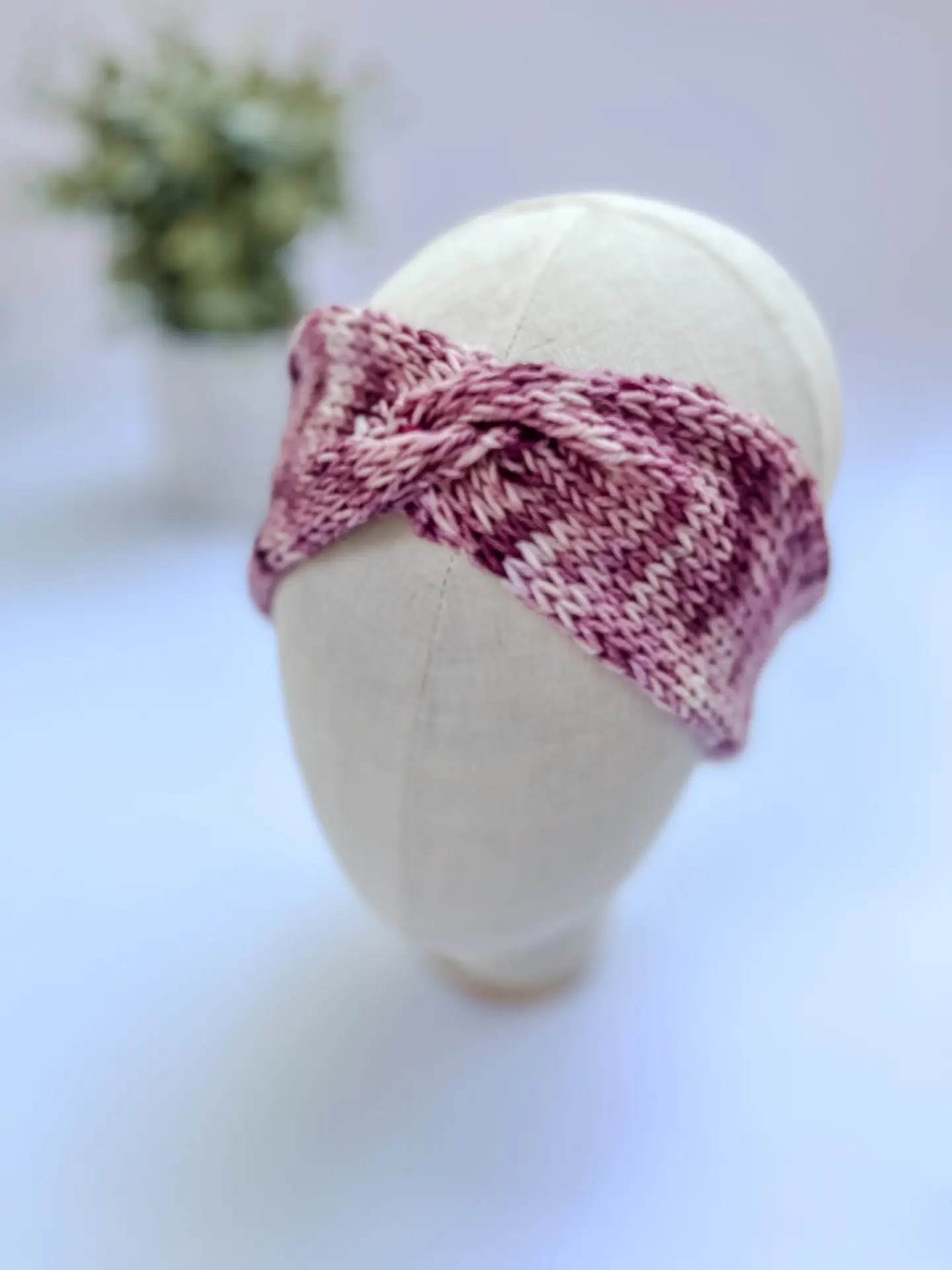 A tonal pink, hand-dyed merino, twisted ear warmer headband is displayed on a cloth mannequin head.