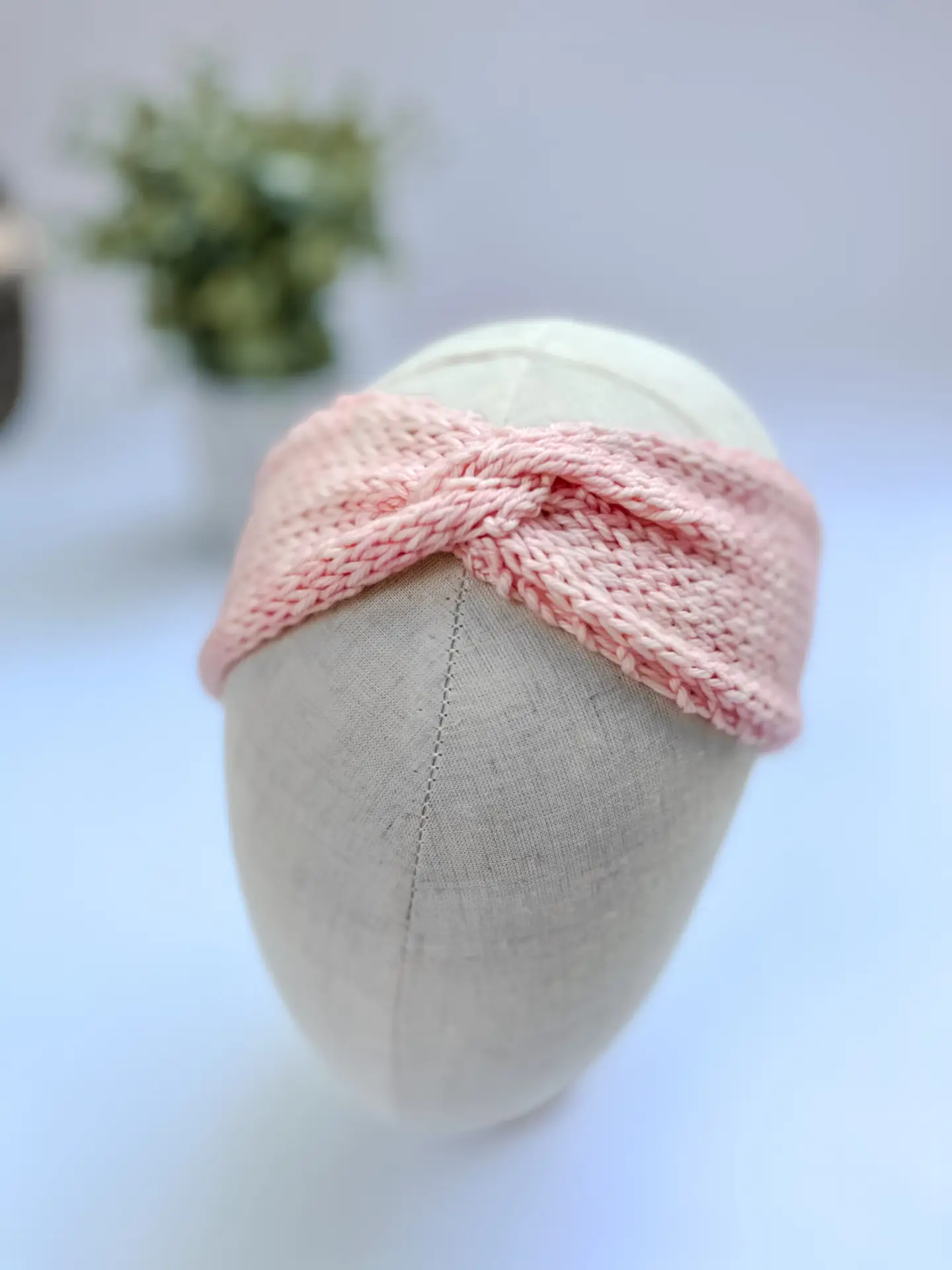 A pink, hand-dyed merino, twisted ear warmer headband is displayed on a cloth mannequin head.