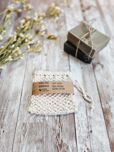 A Virginia-grown cotton soap saver pouch sits next to 2 bars of soap wrapped with twine and a sprig of immature cotton stemsleaves