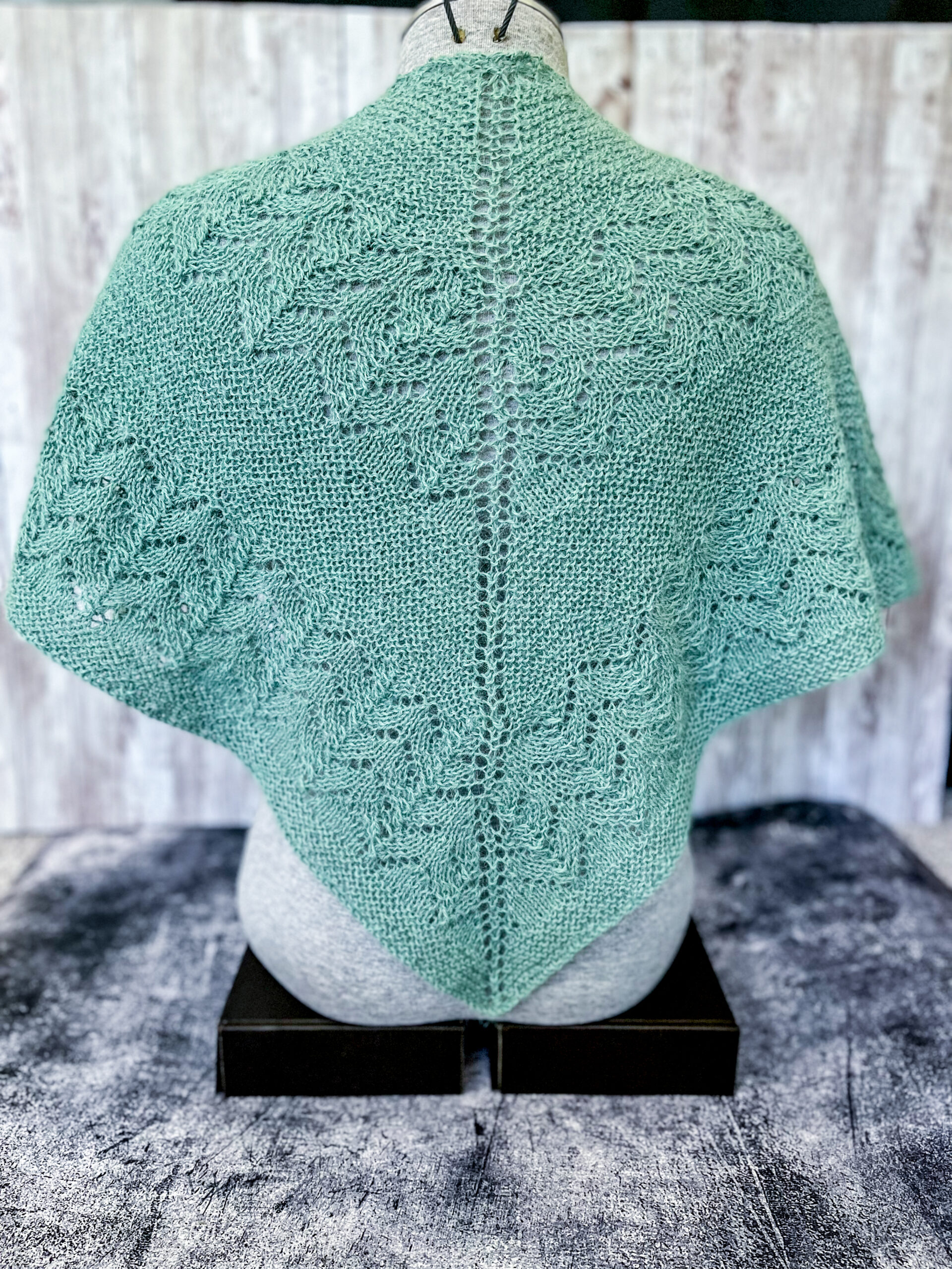 A light eucalyptus green shawl with lace sections alternating with solid sections is shown draped across the back of a mannequin torso.