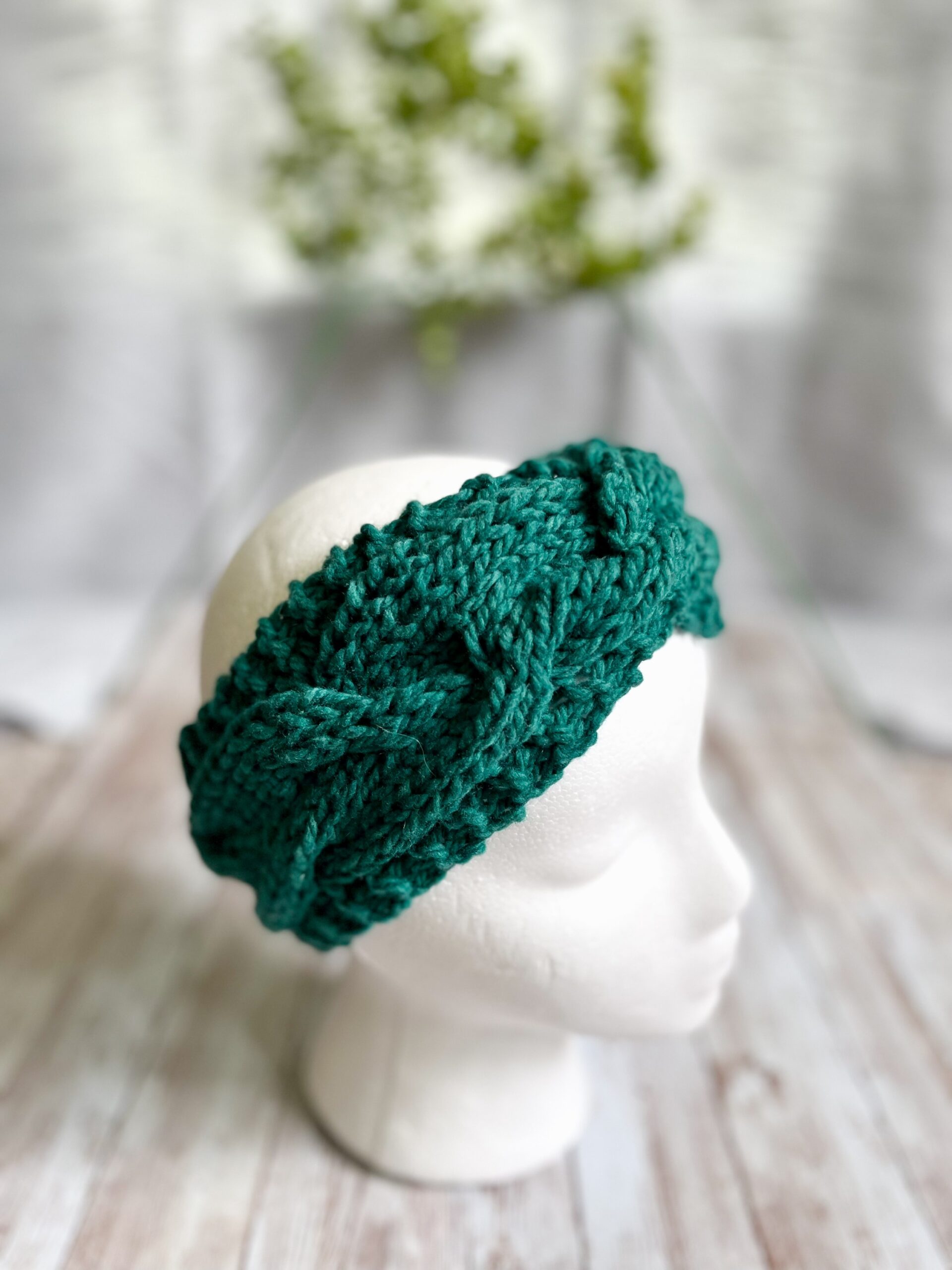 A mannequin head displays a green hand-dyed, Virginia-raised merino cabled ear warmer