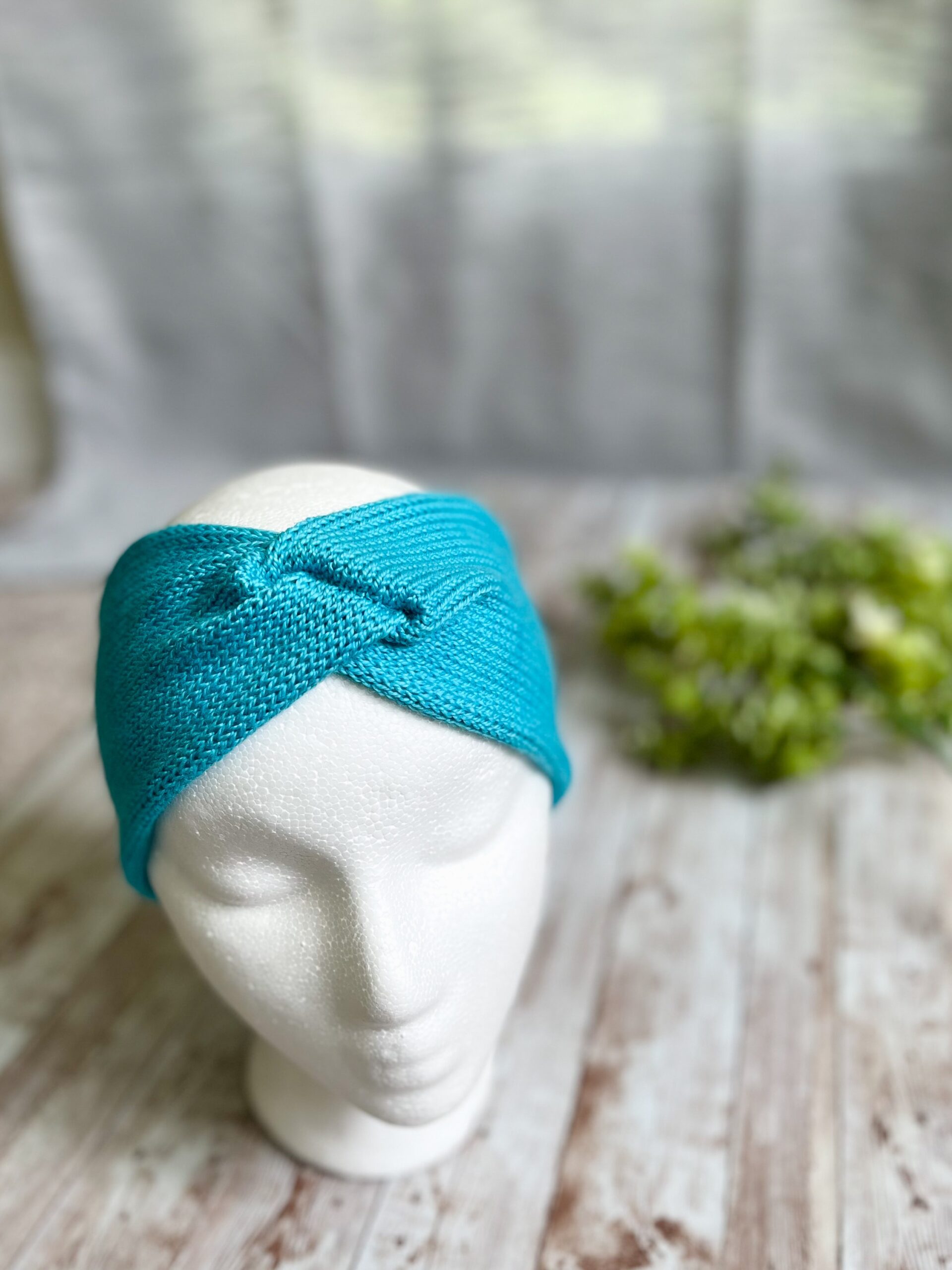 A mannequin head displays a teal hand-dyed merino ear warmer