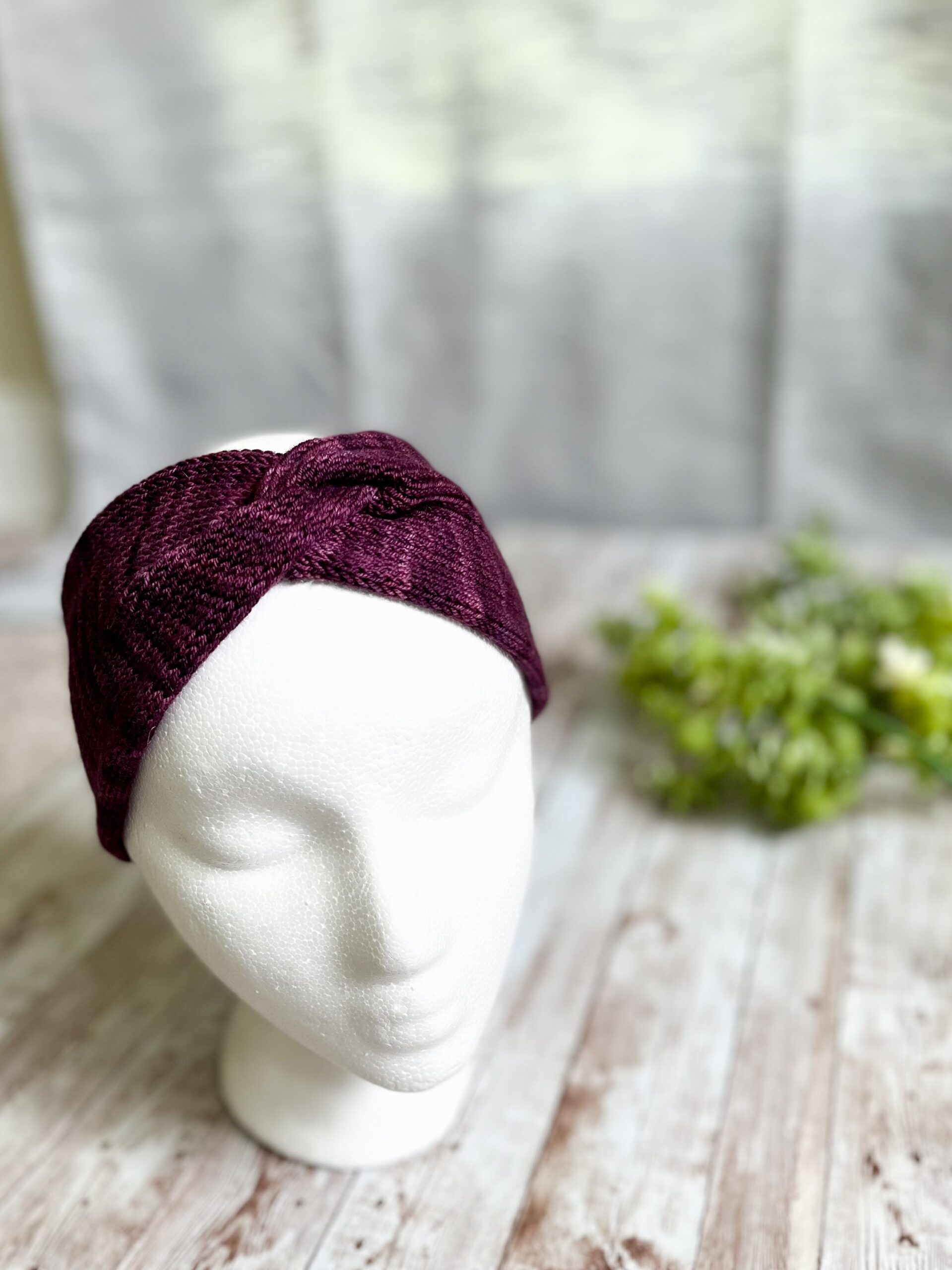A mannequin head displays a plum colored hand-dyed merino ear warmer