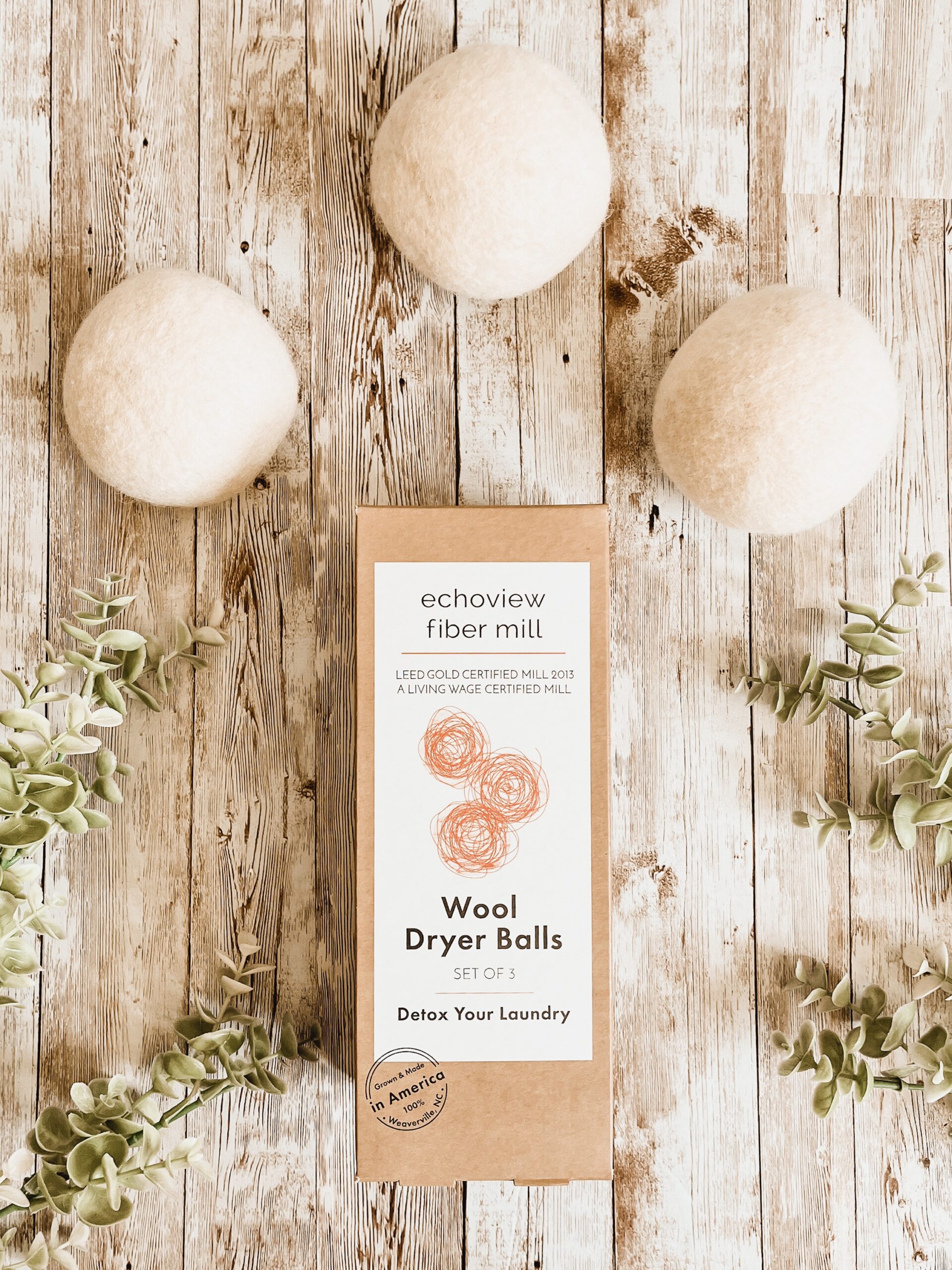 A box of dryer balls is photographed with 3 dryer balls and plants around it