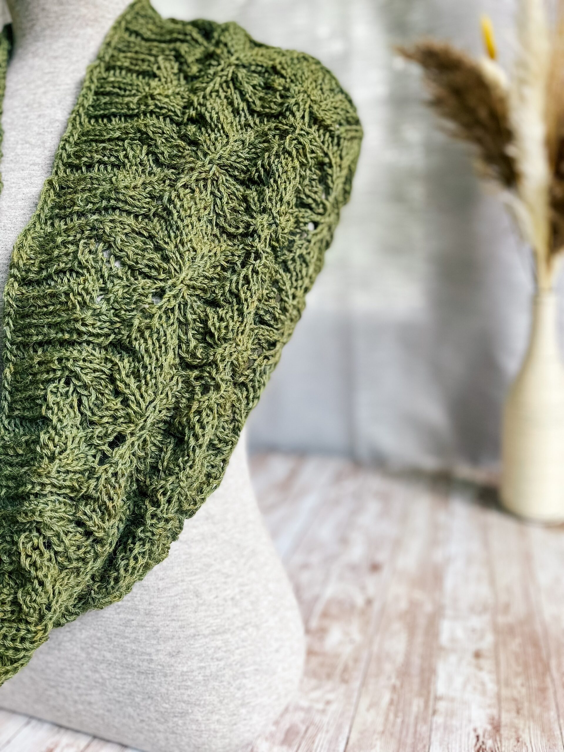 A gray mannequin torso displays a green infinity scarf, hand-knit in a cables and lace pattern