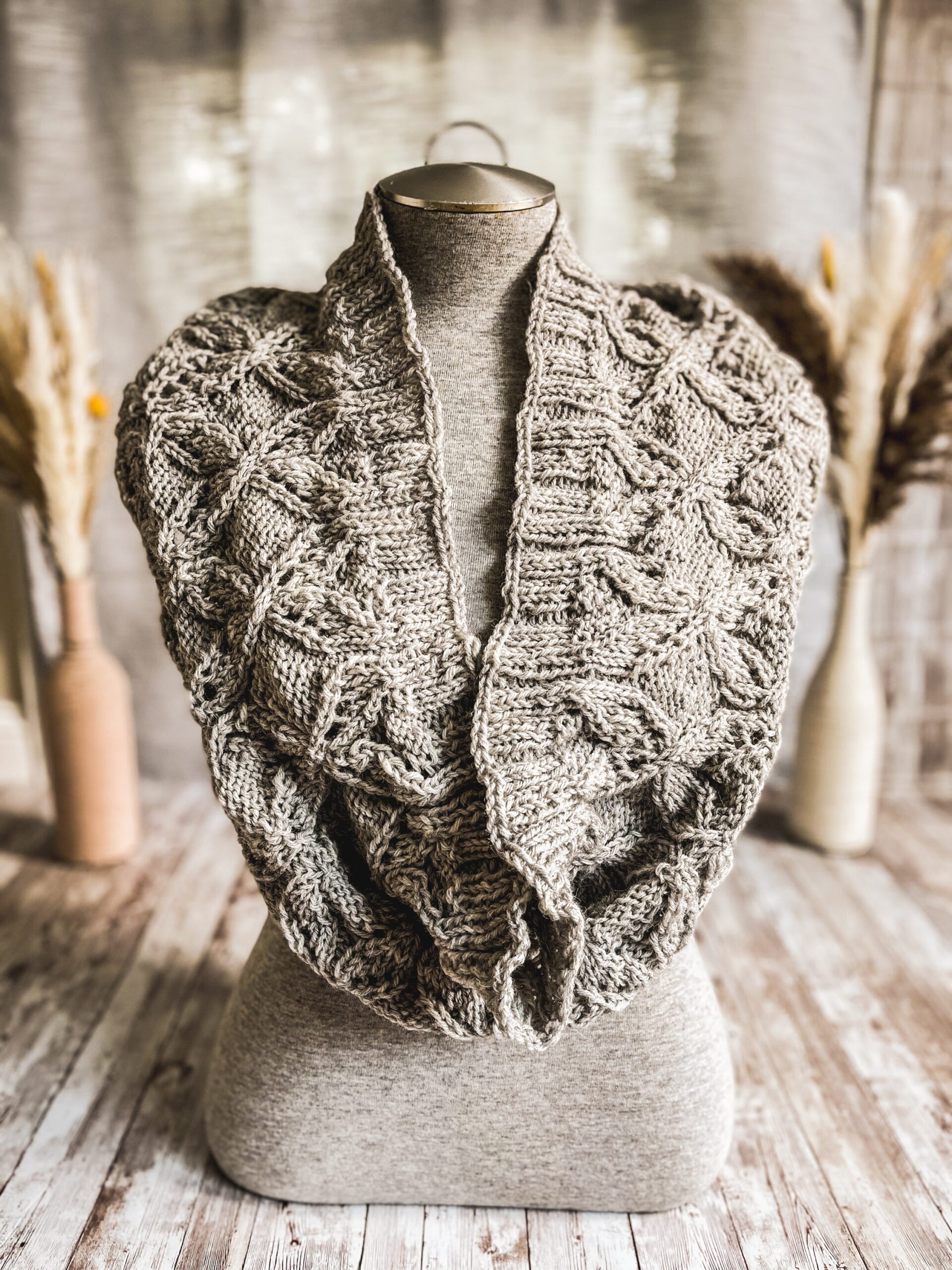 A gray mannequin torso displays a gray infinity scarf, hand-knit in a cables and lace pattern