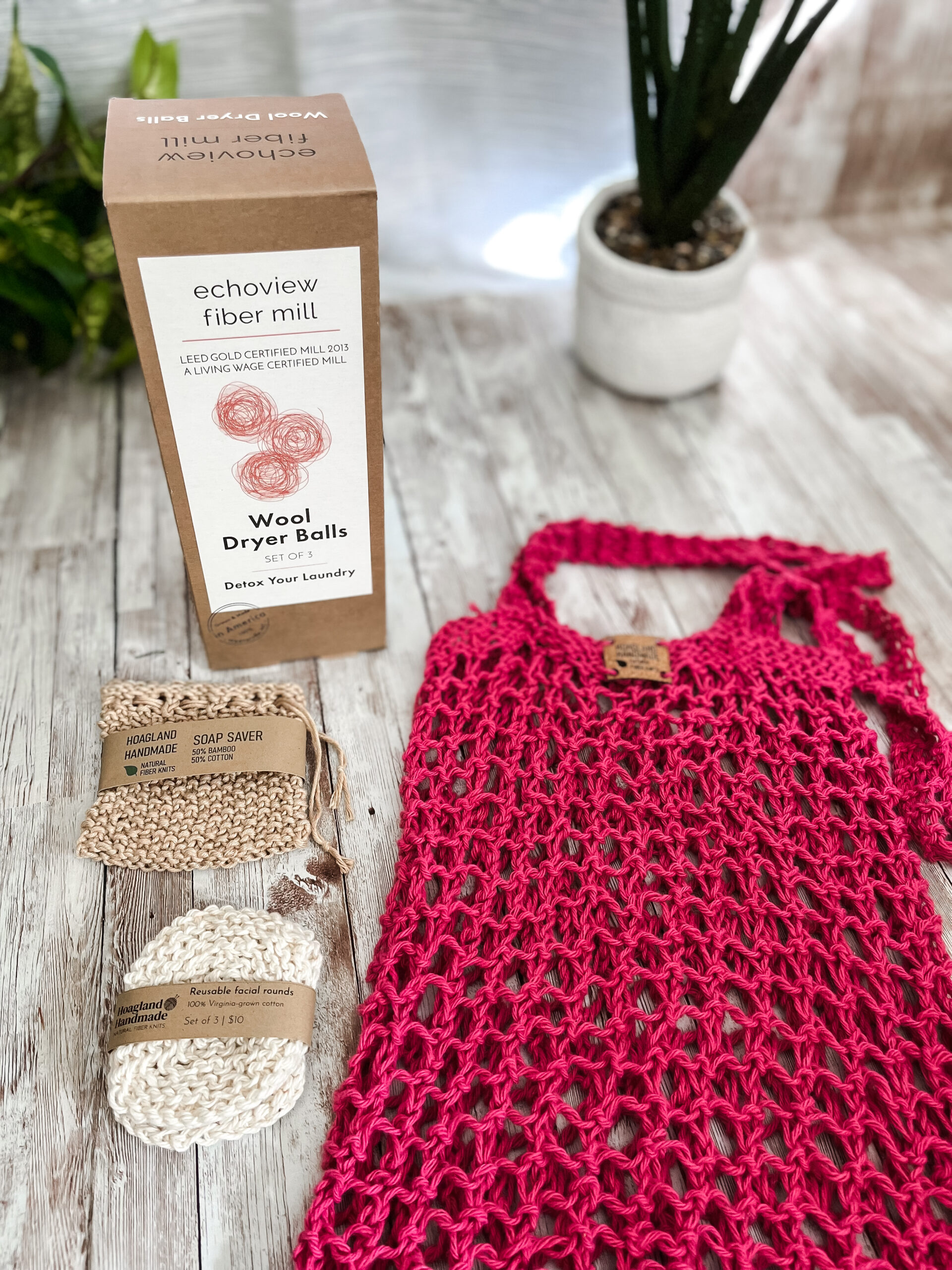 The Zero Waste gift set is pictured showing a box of 3 US Wool dryer balls, a tan bamboo/cotton soap saver pouch wrapped in a kraft paper label from Hoagland Handmade, a set of 3 usable facial rounds knit from Virginia-grown cotton and wrapped in a a kraft paper label from Hoagland Handmade, and a pink recycled cotton knit market tote