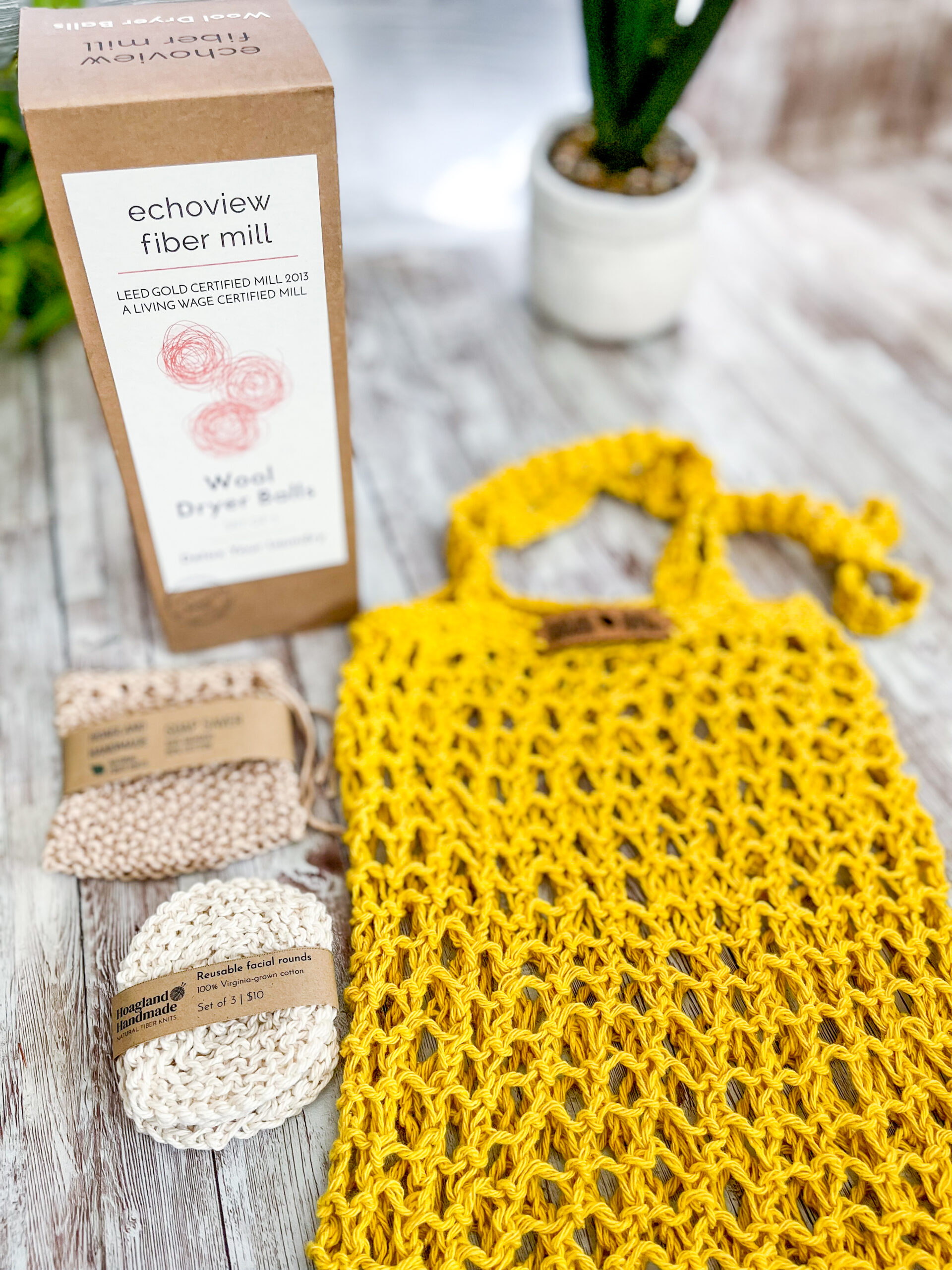 The Zero Waste gift set is pictured showing a box of 3 US Wool dryer balls, a tan bamboo/cotton soap saver pouch wrapped in a kraft paper label from Hoagland Handmade, a set of 3 usable facial rounds knit from Virginia-grown cotton and wrapped in a a kraft paper label from Hoagland Handmade, and a yellow recycled cotton knit market tote
