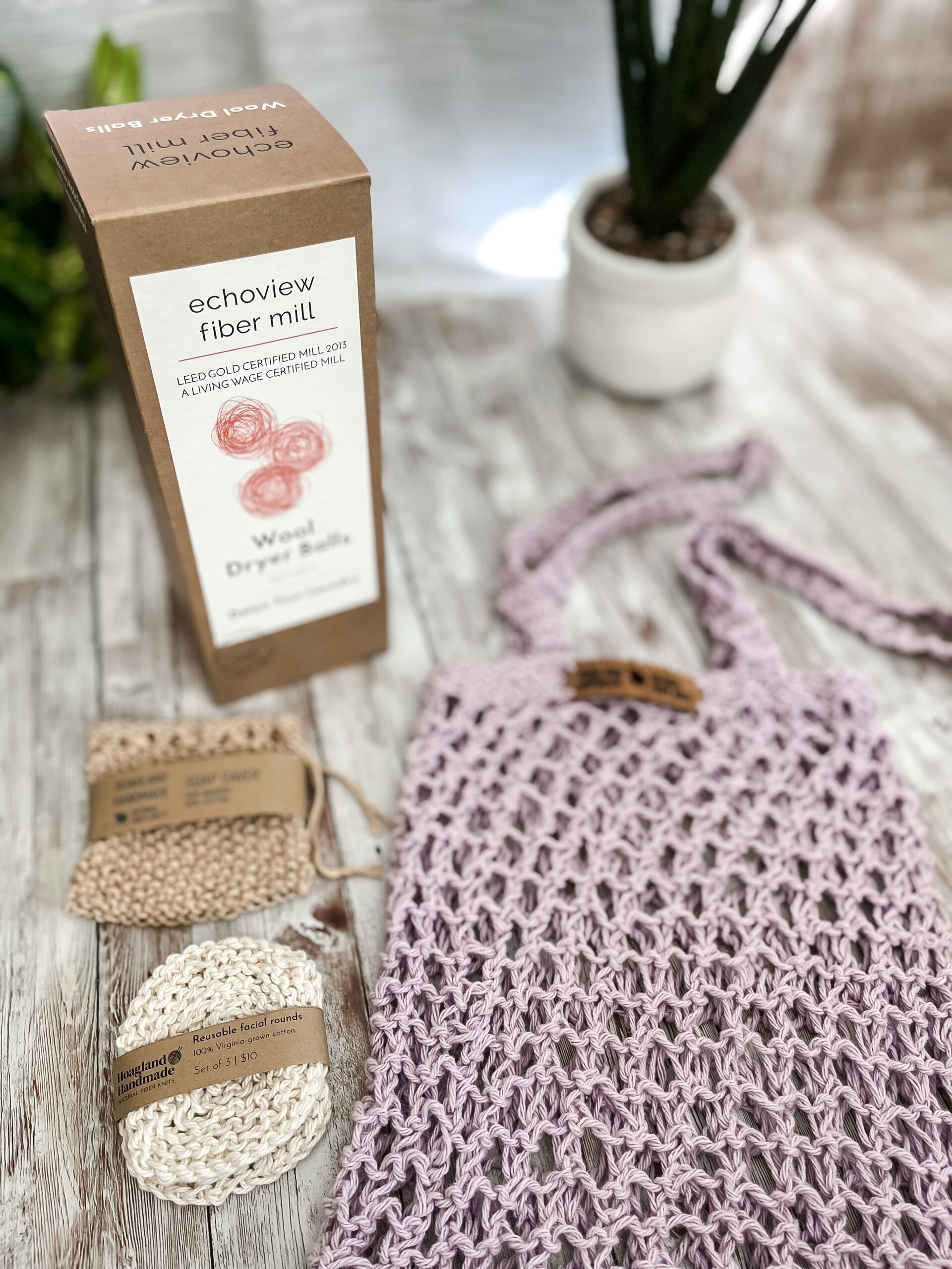 The Zero Waste gift set is pictured showing a box of 3 US Wool dryer balls, a tan bamboo/cotton soap saver pouch wrapped in a kraft paper label from Hoagland Handmade, a set of 3 usable facial rounds knit from Virginia-grown cotton and wrapped in a a kraft paper label from Hoagland Handmade, and a purple recycled cotton knit market tote