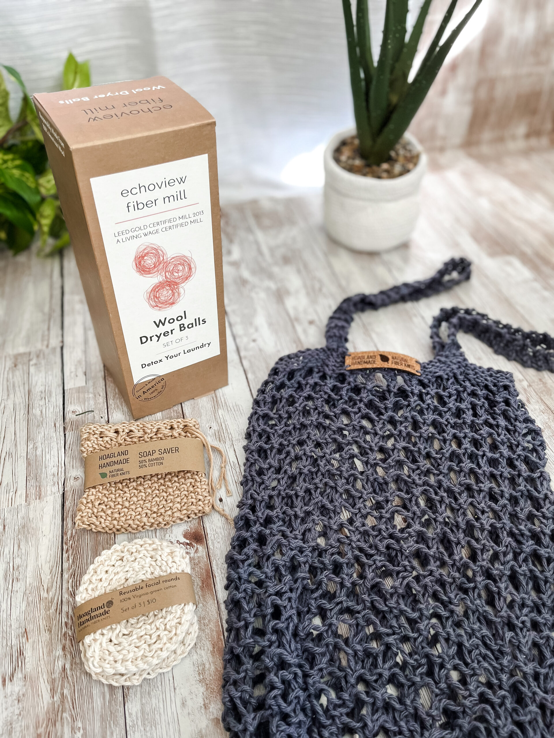 The Zero Waste gift set is pictured showing a box of 3 US Wool dryer balls, a tan bamboo/cotton soap saver pouch wrapped in a kraft paper label from Hoagland Handmade, a set of 3 usable facial rounds knit from Virginia-grown cotton and wrapped in a a kraft paper label from Hoagland Handmade, and a dark blue recycled cotton knit market tote