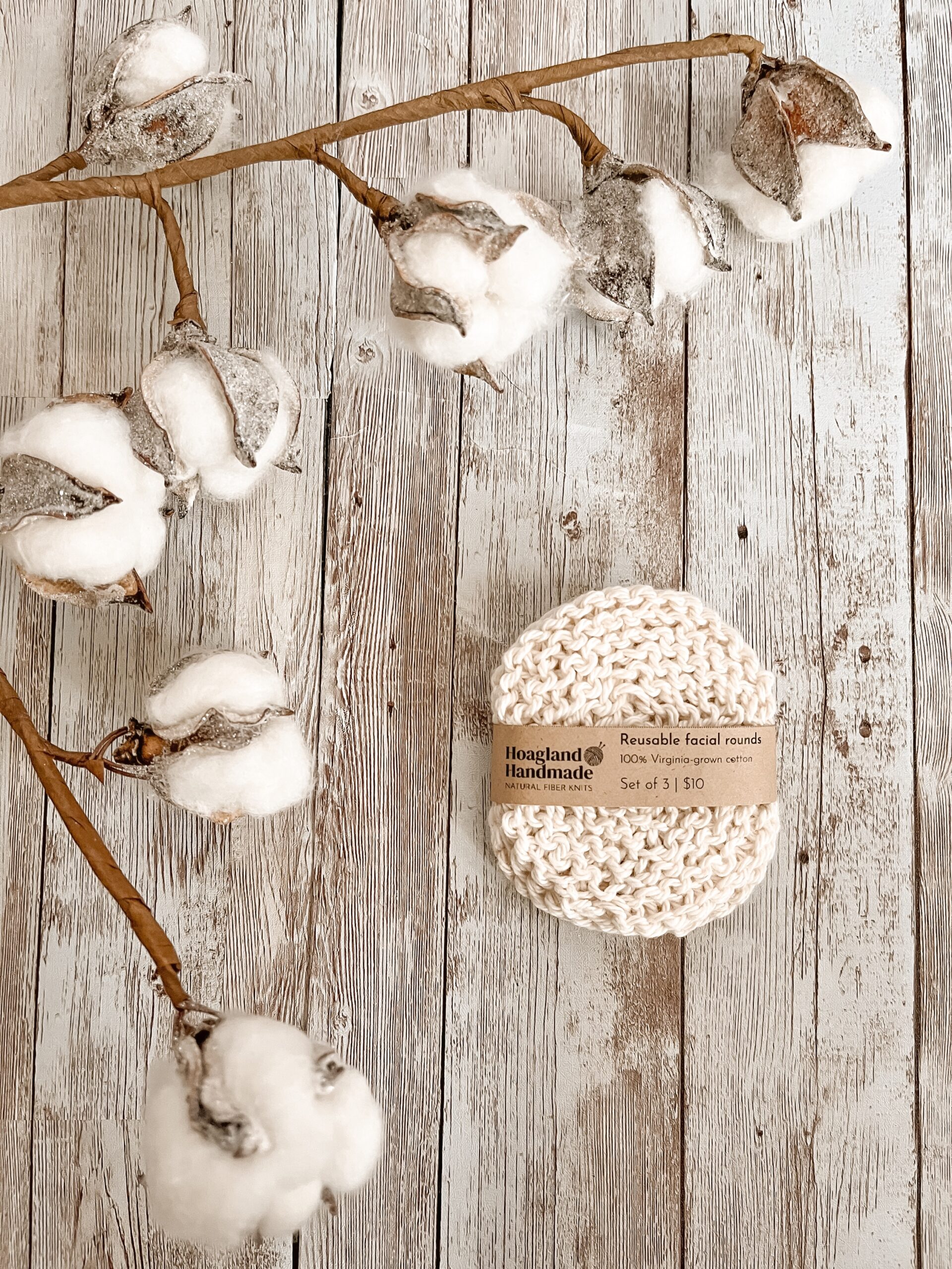 A set of Virginia-grown cotton reusable facial rounds rests on a wood floor, with a cotton stem surrounding the set on the top and left