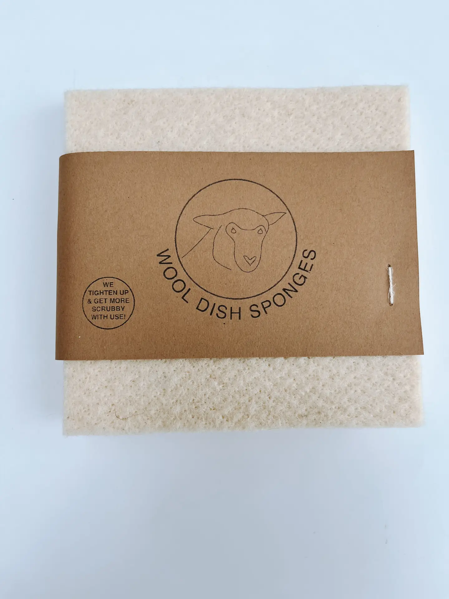 A set of 2 100% wool sponges is shown on a white background. The label includes a sketch of a sheep and the text "We tighten up and get more scrubby with use"